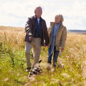 retired-couple-walking-dog-in-field